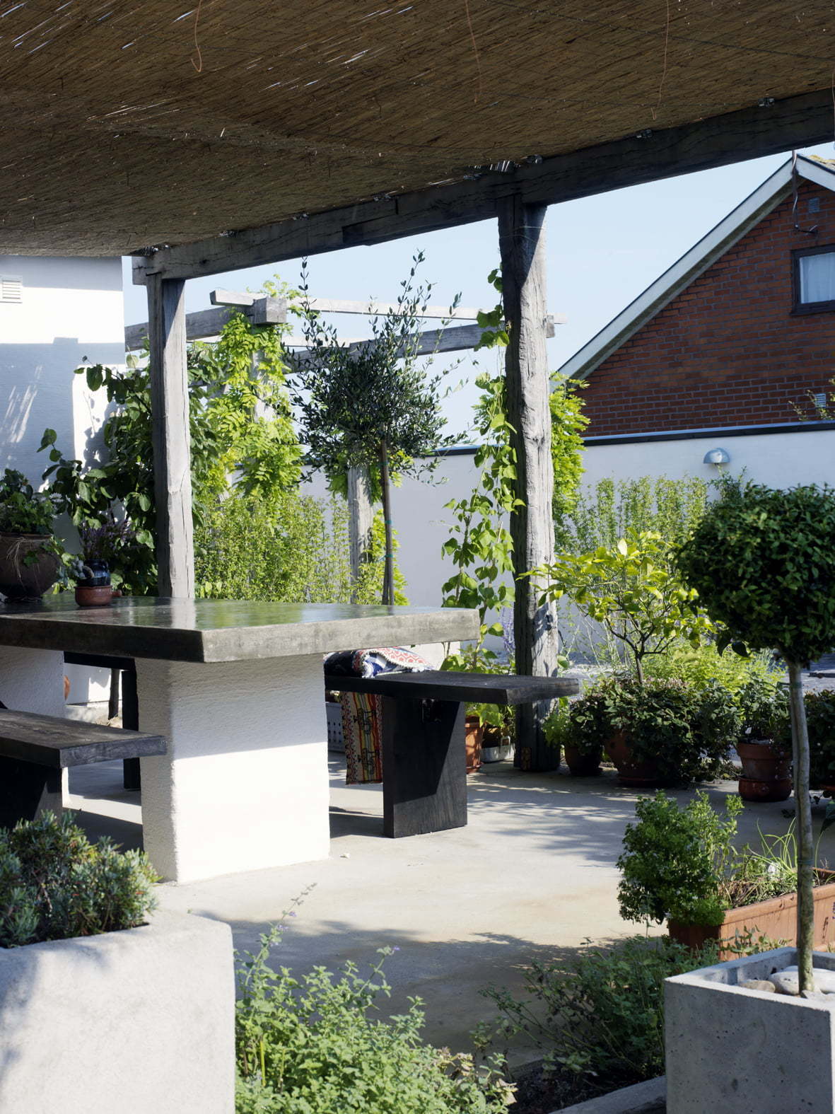 Peter Englander Pergola med vasstak skapar skugga över middagsterrassen i slipad betong.